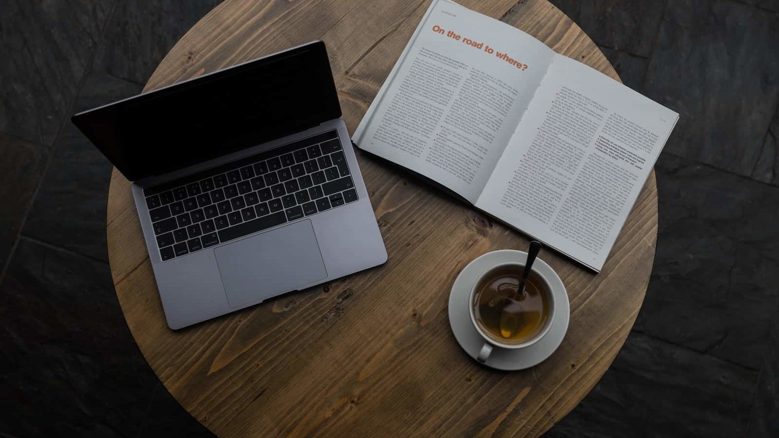 gray laptop beside white teacup and book