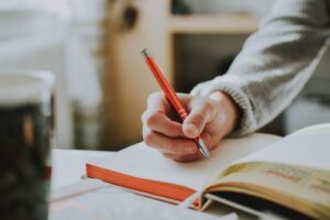 person holding on red pen while writing on book
