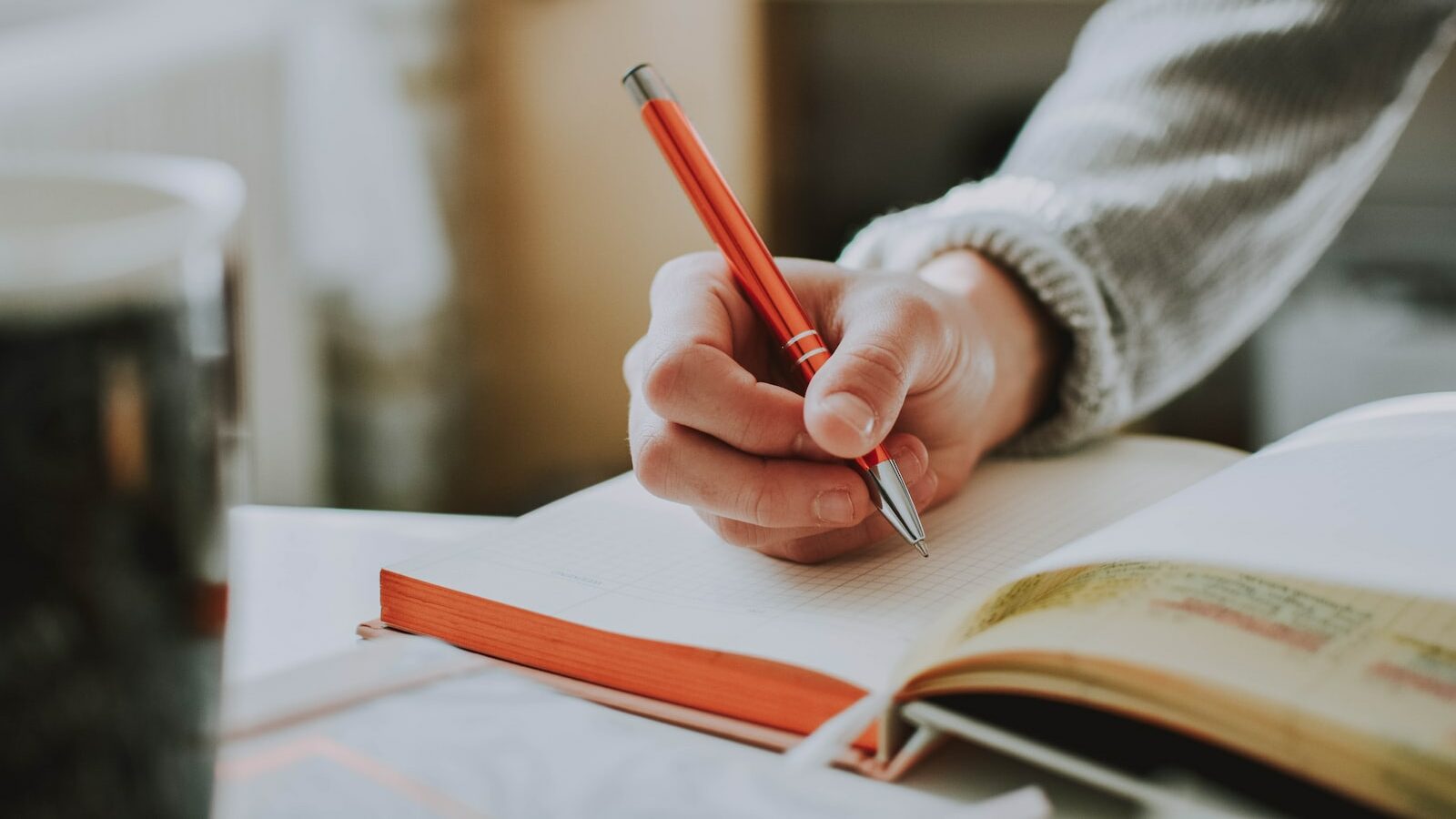 person holding on red pen while writing on book