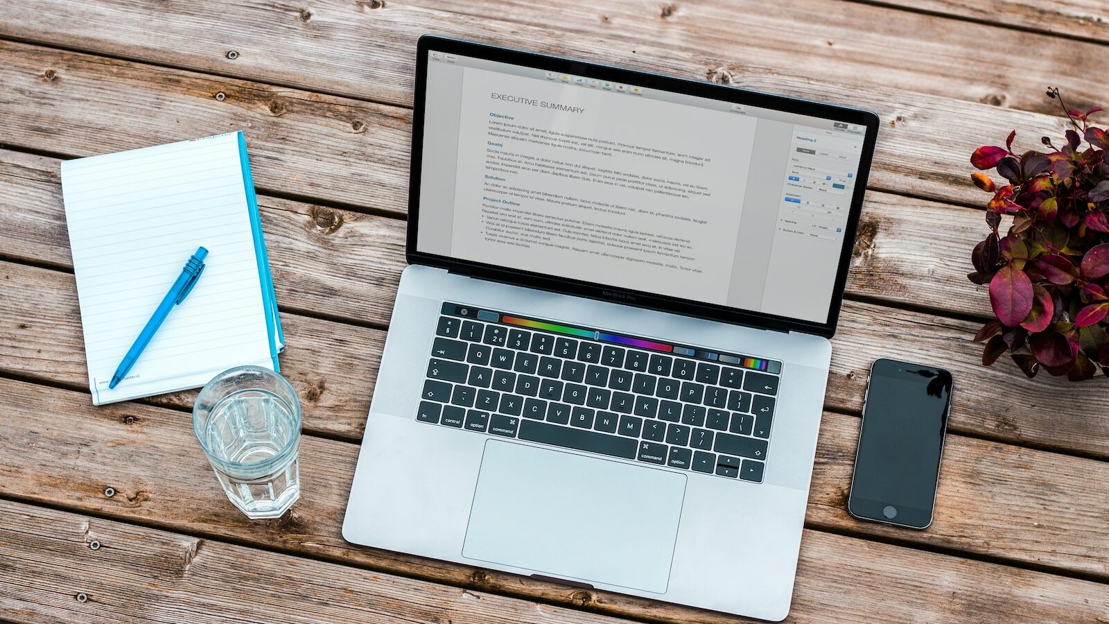 silver MacBook beside space gray iPhone 6 and clear drinking glass on brown wooden top