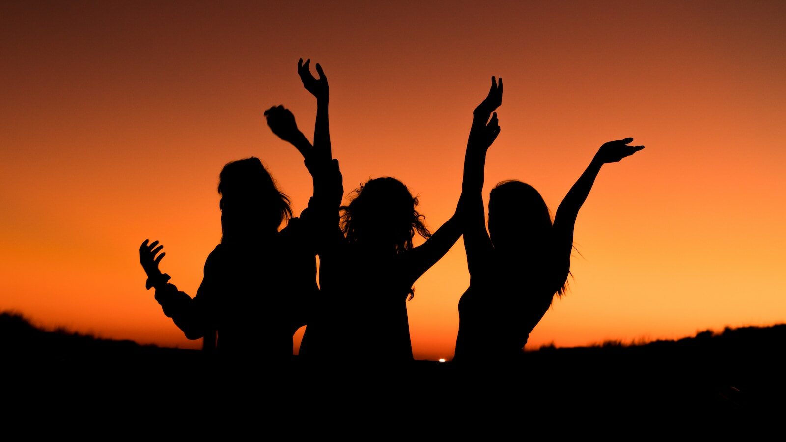 silhouette of three woman with hands on the air while dancing during sunset